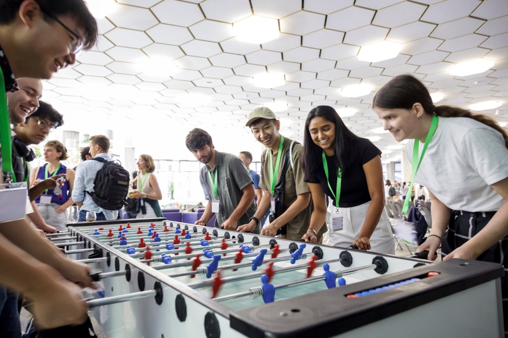 Michael Tan playing on one side of a long foosball table with three teammates against 4 others on the other side.
